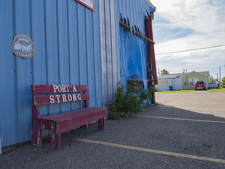 A red bench with "Port A Strong" written on it sits in front of the Port Aransas volunteer fire department building