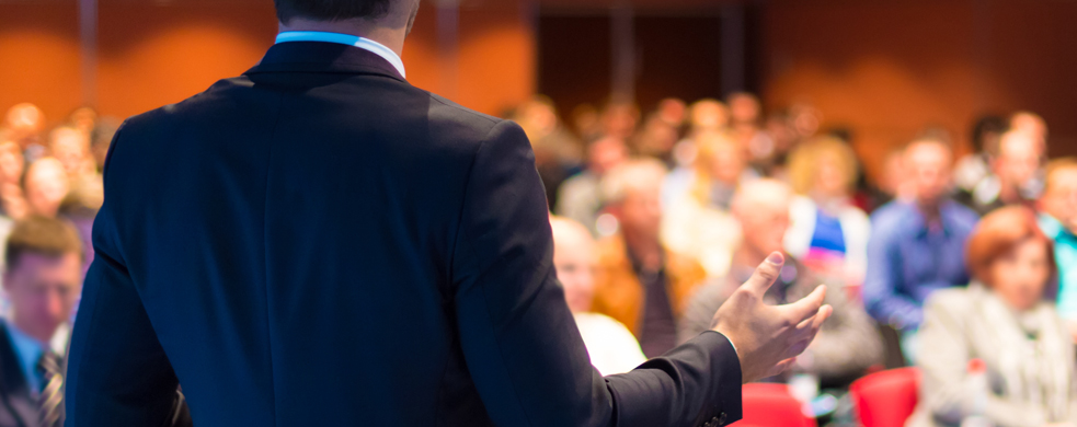 Man in suit in foreground standing in front of audience