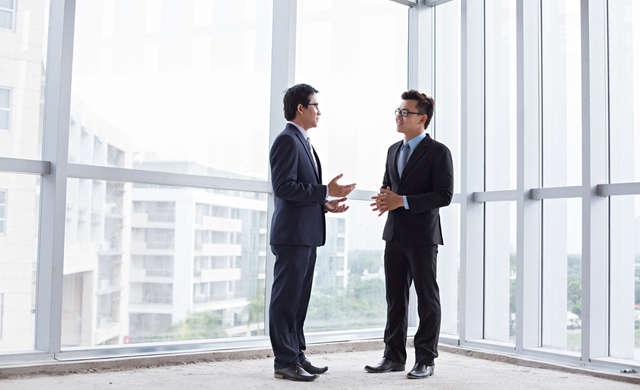 two men in suits talking inside a vacant commercial building