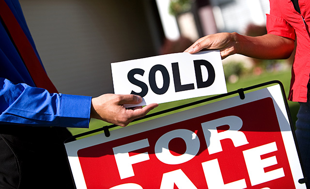 A Texas REALTOR with a client holds a sold sign above a for sale sign in front of a home
